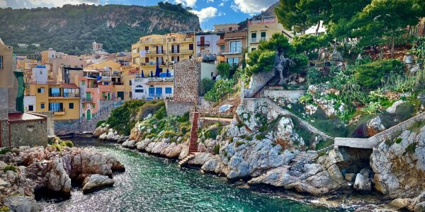 Italian island town with bright coloured houses nestled along a cliffside next to sparkling blue waters.