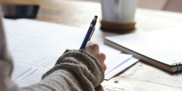 A woman making written notes on a desk with coffee cups and notebooks.